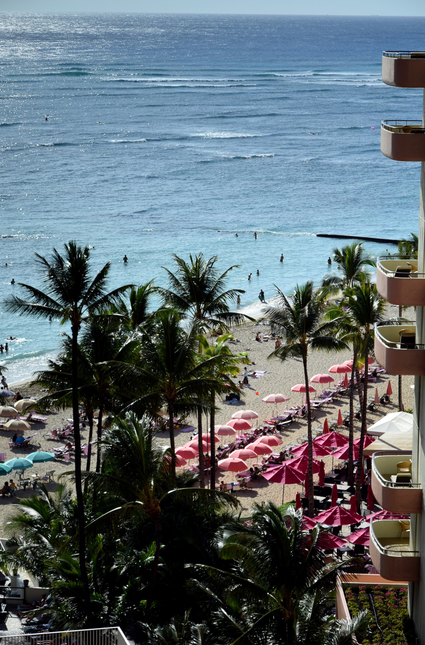 Waikiki Beach with turquoise water, palm trees and pink beach umbrellas below the Royal Hawaiian